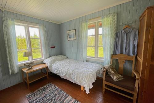 a bedroom with a bed and a chair and two windows at Idyllisk Småbruk in Landsem