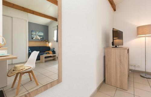 a living room with a television and a chair at Résidence Odalys Le Village des Amareyeurs in Le Château-dʼOléron