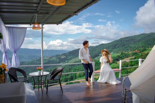 a bride and groom standing on a balcony with a view at ชิวชิวแคมป์ ภูชี้ฟ้า in Ban Huai Han
