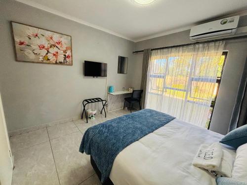 a bedroom with a bed and a window and a desk at Dulelo Guest House Gaborone in Gaborone