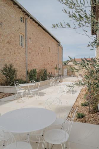 une terrasse avec des tables et des chaises blanches devant un bâtiment dans l'établissement Château du Bost, 21 personnes, piscine, Beaujolais, Blacé proche Lyon, à Blacé