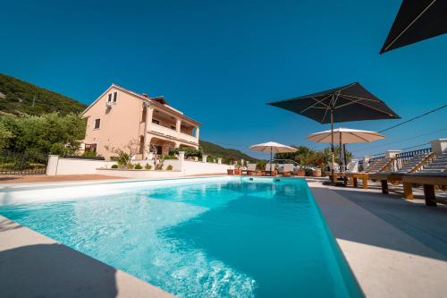 a swimming pool with umbrellas and a house at Villa Mianka Rab in Banjol