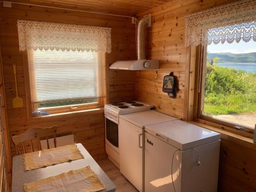 a kitchen in a log cabin with a stove and two windows at Søndre Forøya Gård in Tromsø