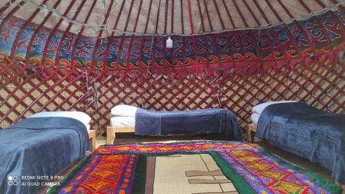 a yurt with three beds and a rug in it at Ernis Yurt Camp in Mineralʼnyy Istochnik Altyn-Arasan