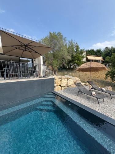 une piscine avec un parasol et des chaises ainsi qu'une maison dans l'établissement La villa du Clos, à Saint-Paul-de-Vence