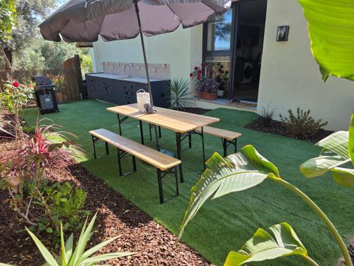 a picnic table and bench under an umbrella in a garden at Casa de ferias escapadas casa amorosa Tranquilidade e natureza 2 quartos 6 pessoas in Loulé