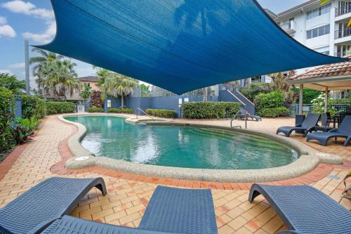 a swimming pool with two chairs and a blue umbrella at Tropical Comfort Pool and Stunning Esplanade in Cairns