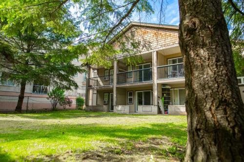 a large building with a tree in front of it at The Flats at Cedar Springs with Full Kitchen and Steps to Lake in Harrison Hot Springs