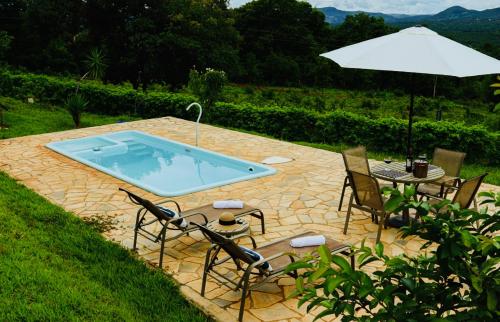 Un patio con piscina, sillas y sombrilla. en Estância do Sol, en Pirenópolis