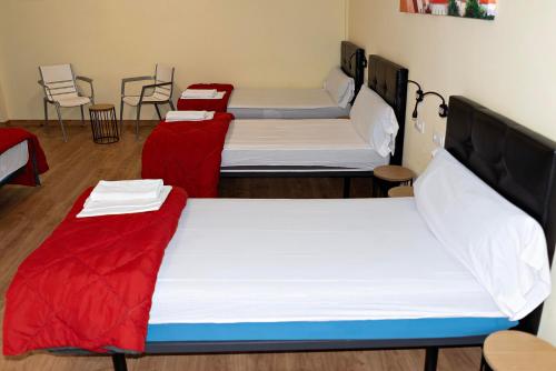 a room with three beds with red and white sheets at Cruce de Caminos Arzúa in Arzúa