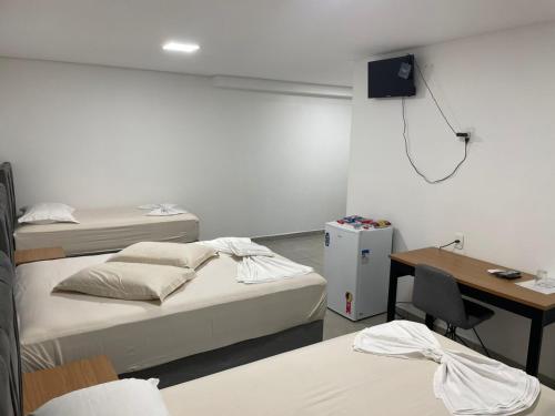 a room with two beds and a desk with a computer at Hotel Califórnia Cruz Alta in Cruz Alta