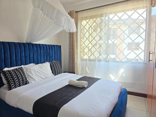 Un dormitorio con una cama con cabecero azul y una ventana. en Marie's 2 bed all-ensuite Milimani ksm, en Kisumu