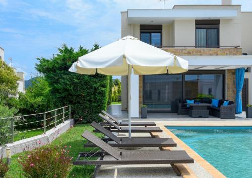 an umbrella and lounge chairs next to a swimming pool at Pentanemi Luxury Villa in Hanioti