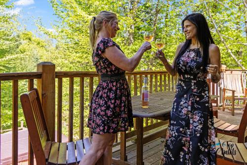 Dos mujeres de pie en una terraza sosteniendo copas de vino en Log Cabin Hot tub near Tremblant, en Labelle