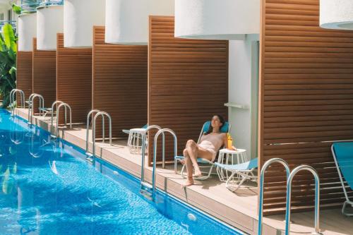 a woman sitting in a chair next to a swimming pool at Flora Garden Ephesus Kusadasi - All Inclusive in Davutlar