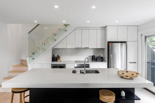 a white kitchen with a sink and a staircase at Arya in Byron Bay