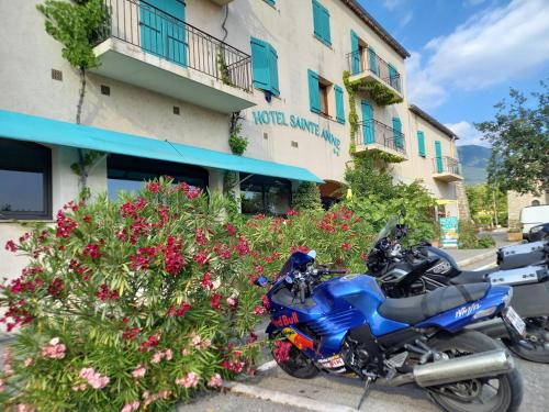 une moto bleue garée devant un bâtiment avec des fleurs dans l'établissement Hôtel Sainte Anne 
