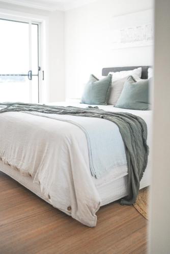 a white bed with white sheets and green pillows at Diggers Beach Villa Coffs Harbour in Coffs Harbour