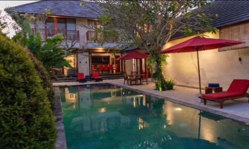 ein Swimmingpool mit roten Stühlen und einem Sonnenschirm in der Unterkunft Enchanting Canggu Villa in Tumbak Bayuh