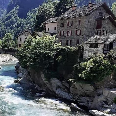 a building on a hill next to a river at Ground floor apartment with garden in Campertogno