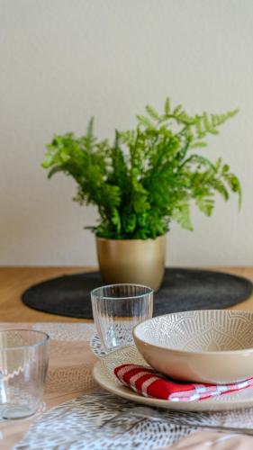 a table with plates and glasses and a potted plant at Appartement Cosy - Résidence avec Parc et Piscine in Marans