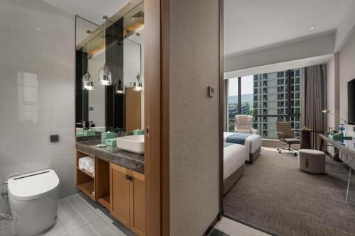 a bathroom with a sink and a toilet and a bedroom at Hangzhou Qiantang Shama Hotel in Hangzhou