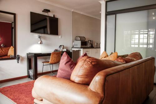 a living room with a brown leather couch with pillows at Yalla Yalla Boutique Hotel in Witbank