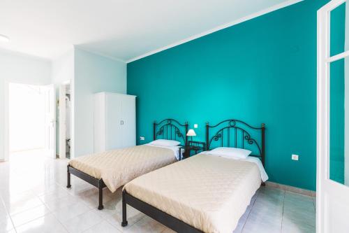 two beds in a room with a blue wall at Fexulis Studios & Suites in Agios Nikolaos
