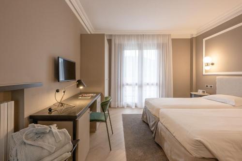 a hotel room with two beds and a desk and a television at Hotel Apollo Terme in Montegrotto Terme