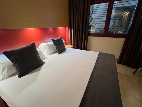 a large white bed with two black pillows on it at Wuau! Hotel Galanthus & Spa in Soldeu