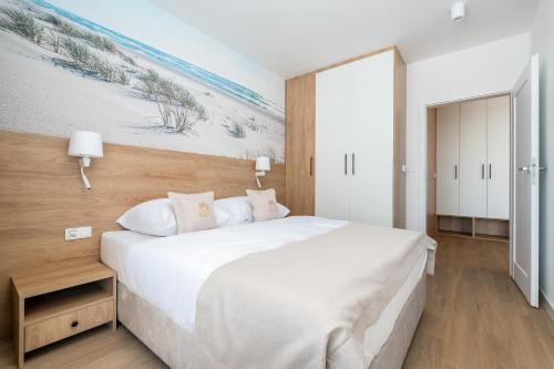 a bedroom with a large white bed with a painting on the wall at Sarbinove City Apartments in Sarbinowo