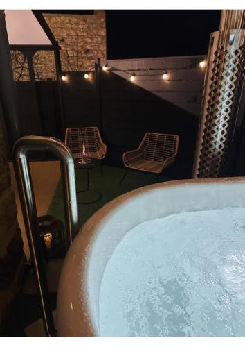 a bath tub on a balcony with a table and chairs at La Cachette du Domaine du Moulin avec son spa privé en option in Saint-Laurent-dʼAndenay