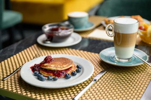 a plate of pancakes and berries next to a cup of coffee at Grand Hotel Esztergom in Esztergom