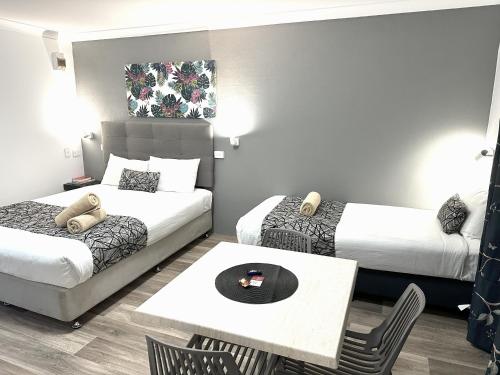 a hotel room with two beds and a table at Rosebourne Gardens Motel in Woolgoolga