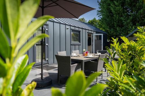 a table with chairs and an umbrella in front of a shed at Moderne Tiny Chalet, 15min van Zeeuwse Kust VP072 in Heinkensand
