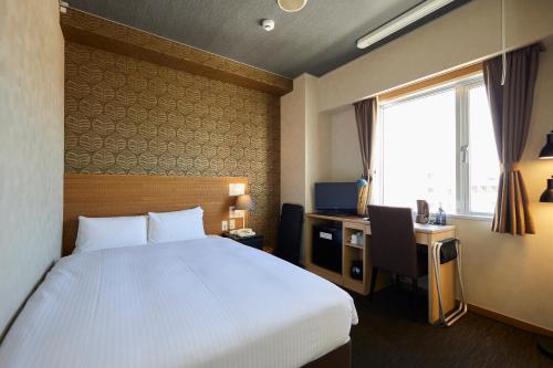 宮古島にあるSmile Hotel Miyakojimaのベッドと机と窓があるホテルの部屋