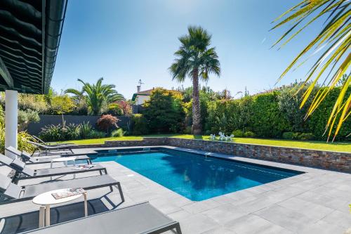 a swimming pool with chairs and a palm tree at Villa Julia - Villa contemporaine avec piscine in Anglet
