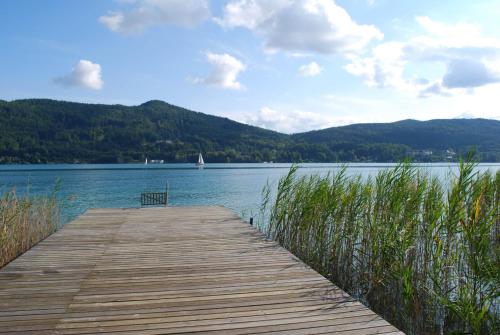 a wooden dock with a bench sitting on top of a lake at Haus Elisabeth, Appartements in Krumpendorf am Wörthersee