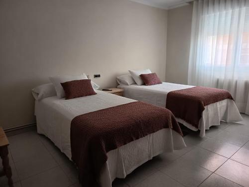 two beds in a white room with a window at Hotel Alejandrina Poio in Poio