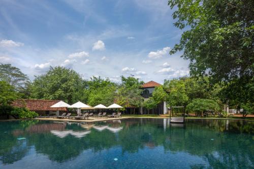 a large swimming pool with tables and umbrellas at SigiriyaJungles Resort & Spa in Sigiriya