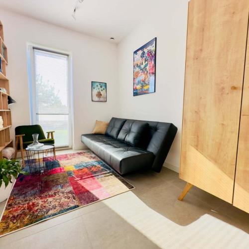 a black leather couch in a living room with a rug at LasMinute - stodoła z prywatną balią in Kazimierzów