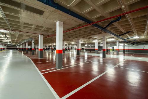 an empty parking garage with a red floor and white columns at Hotel Diagonal Plaza in Zaragoza