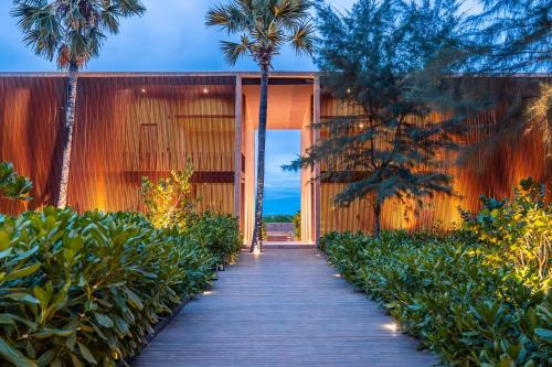 a wooden walkway leading to a building with palm trees at inchantreedoolay huahin in Pran Buri