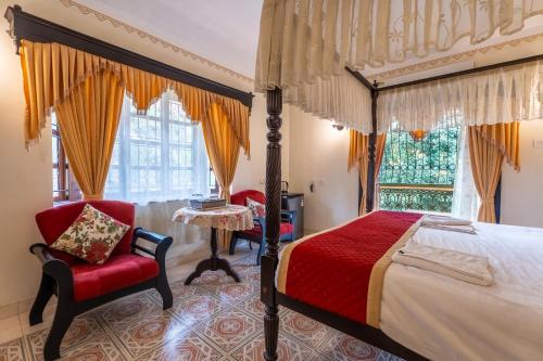 a bedroom with a canopy bed and a red chair at Palm Grove Cottages - Leisure Resort in Benaulim