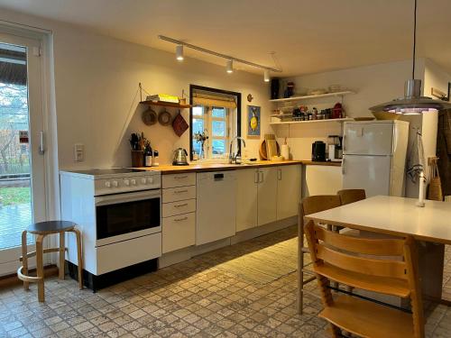 a kitchen with white appliances and a table and a dining room at Be Surrounded By Trees In A Thatched Cottage in Nykøbing Sjælland