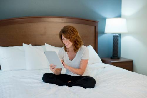 a woman sitting on a bed looking at a tablet at AmericInn by Wyndham Pampa Event Center in Pampa