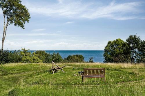 a bench and a picnic table in a field with the ocean at Home By Beach With Panoramic Views in Nykøbing Sjælland