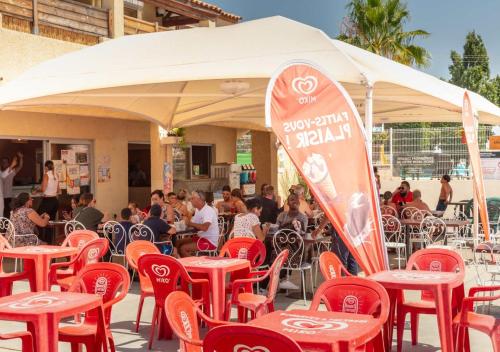 un groupe de personnes assises à des tables sous une tente avec une planche de surf dans l'établissement Camping Les Salins de la Gardiole - Eurocamp I Homair, à Vic-la-Gardiole