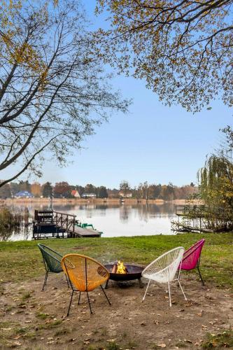 three chairs sitting around a fire pit next to a lake at Cozy Wooden House By The Lake in Falkensee