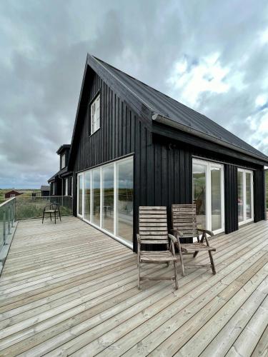 ein schwarzes Haus mit zwei Stühlen auf einer Holzterrasse in der Unterkunft Luxury With Pool In Dunes Near Løkken in Løkken